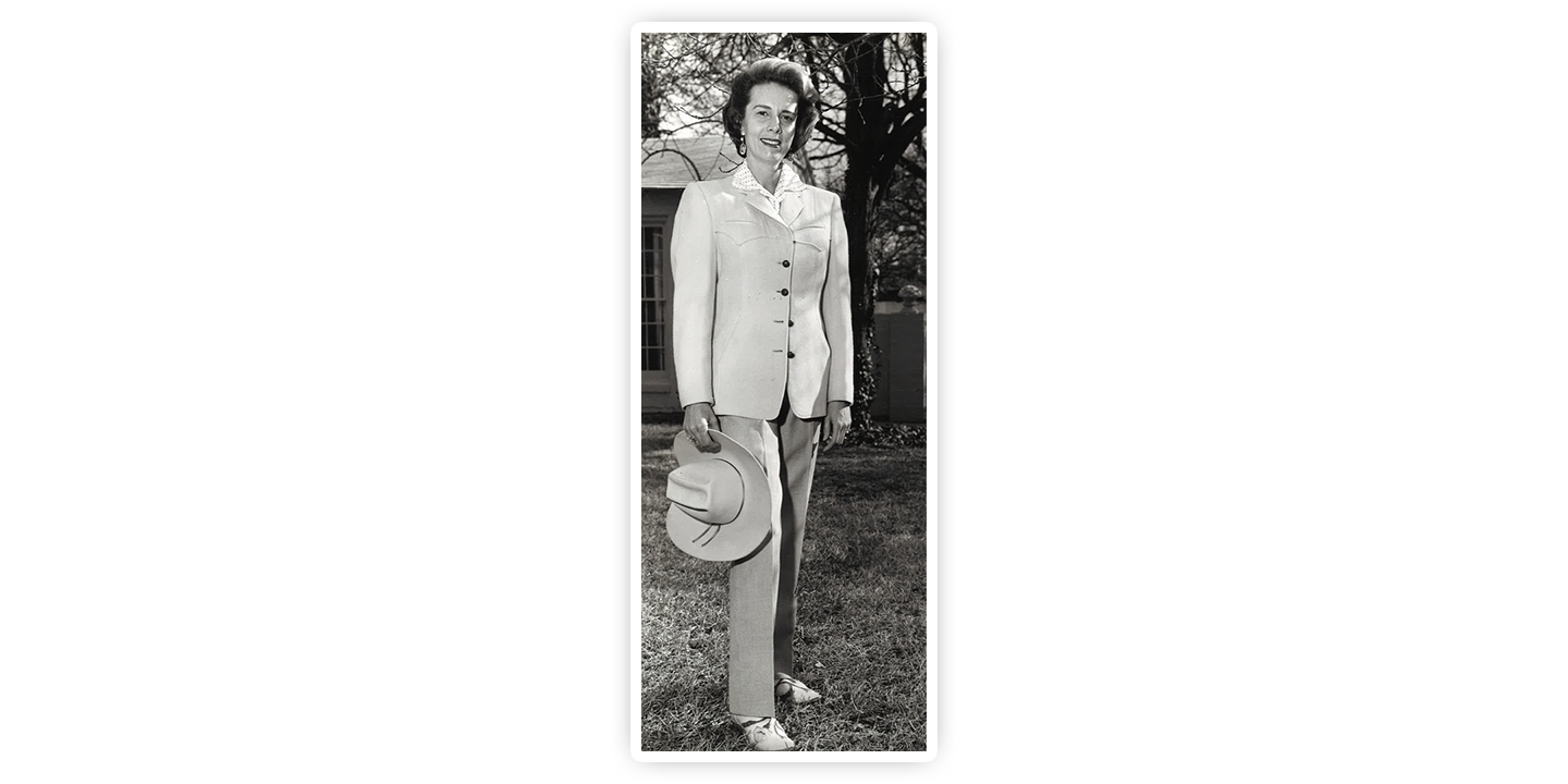 A young Jane Chilton Justin posing in the grass holding a cowboy hat and wearing a business suit.